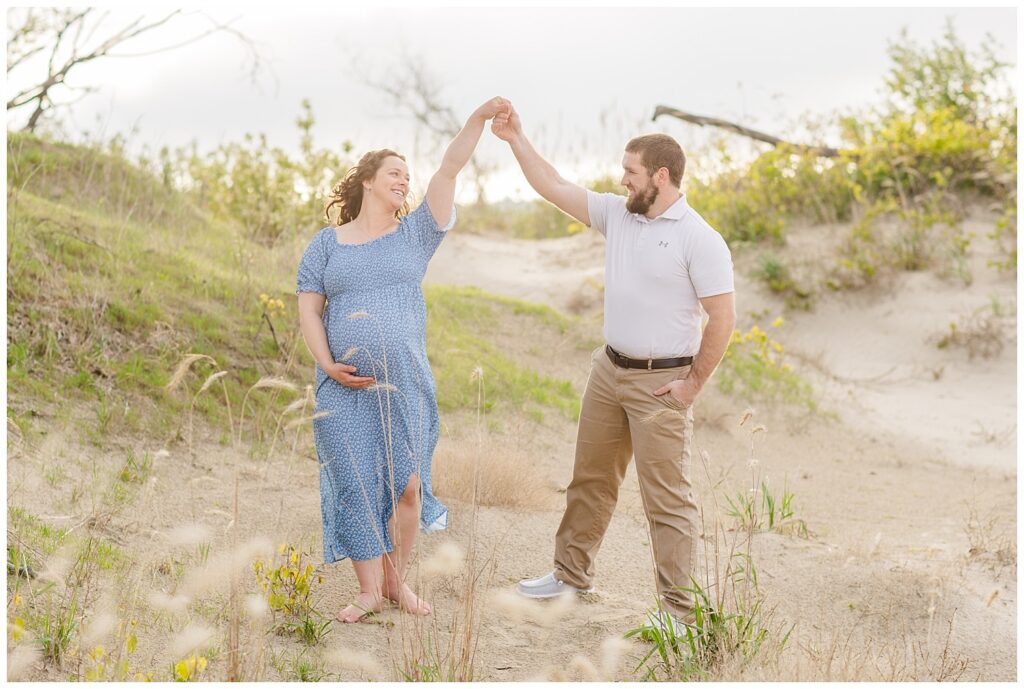 husband twirling his pregnant wife on the beach at Lake Erie for maternity session
