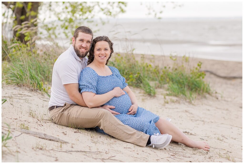 husband and wife sitting together on the beach for maternity session with East Harbor State Park photographer
