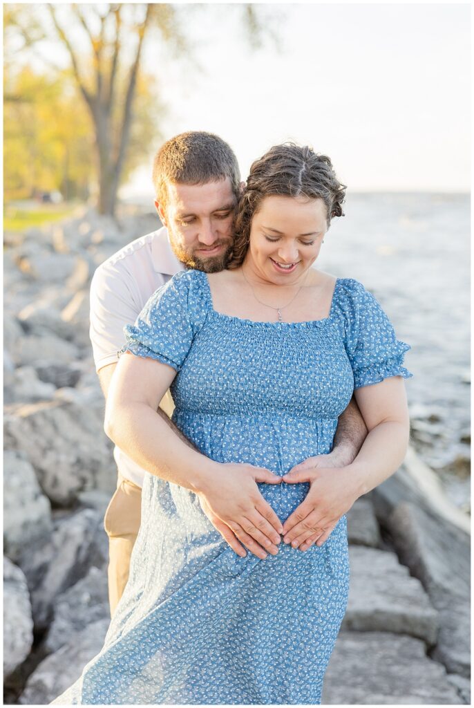 married couple making the shape of a heart on wife's belly during Lake Erie maternity session