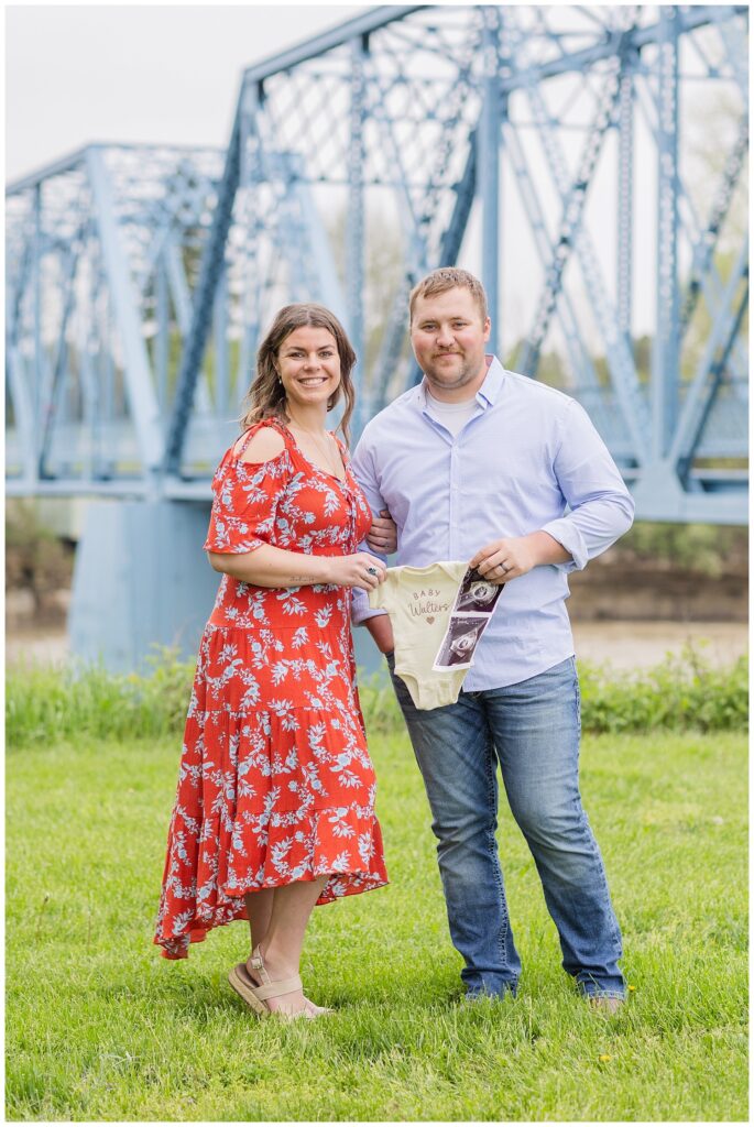 married couple holding a sonogram picture and onesie to announce their pregnancy